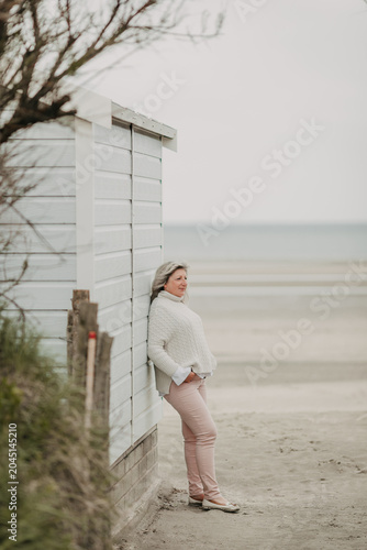 Canvastavla mature woman relaxing by white beach hut among dune grass on quiet coast