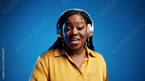 Joyful woman listening to music and dancing on blue background