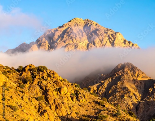 Sunlit Rocky Mountain Peak Rising Above Cloud Layer Under Clear Blue Sky