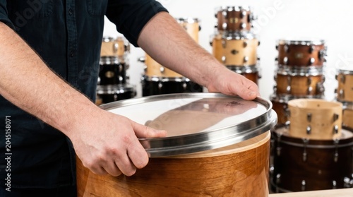 Drum maker hands carefully placing a new clear drumhead onto a finished wooden drum shell in a workshop