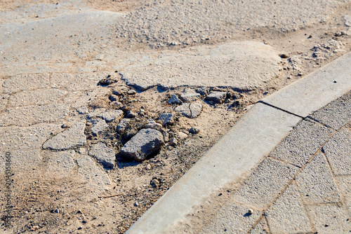 Tableau sur toile Cracked pavement with asphalt erosion near concrete curb on sunlit street
