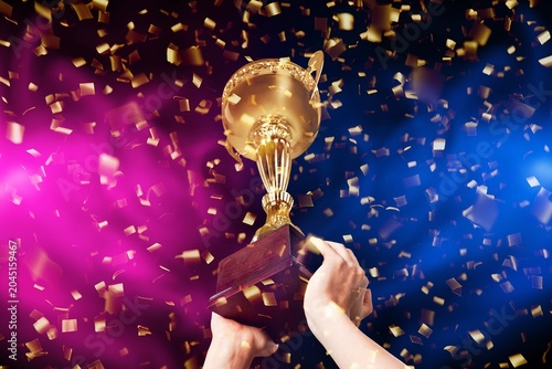 Foto Gold trophy cup held by hands with falling confetti and colorful lights during a