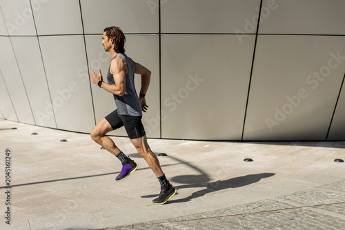 Fotografie Man runs swiftly along a modern building under bright sunlight