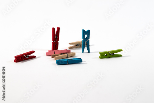 An assortment of colorful blue, green, red and natural plain wooden clothespins on a clean white background.