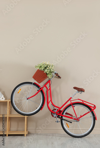 Bicycle with basket of beautiful wildflowers and shelving unit near beige wal...