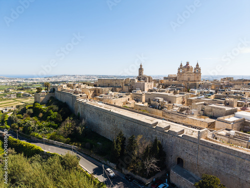 Aerial view of the historic fortified city of Mdina with its massive stone bastions, St. Paul's Cathedral, and limestone architecture under a clear blue sky in Mdina, Western Region, Malta.