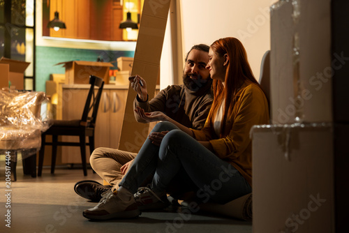 Obraz na plátně Holding keys, happy couple, home ownership, buying new house, celebrating life event together, Partners taking a break from moving and sitting on the floor, admiring their achievement