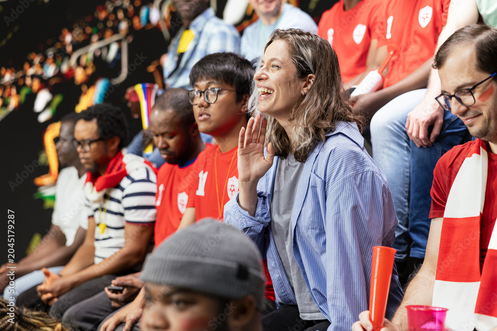 Obraz premium Passionate woman football supporter cheering with red team crowd in stadium stands during intense soccer match, football equality and inclusion. Sports fans celebrate with chants.