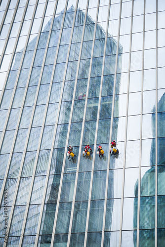 Professional window cleaners working on the exterior of a modern glass skyscraper using rope access techniques, highlighting building maintenance, safety equipment, and high-rise urban services