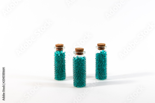 Three small clear glass bottles with cork stoppers filled with green beads on a white background