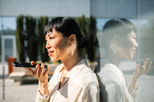 Businesswoman using voice assistant on smartphone outside office