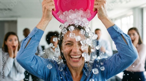 Broken ac office funny workplace concept: overheated businesswoman pouring a bucket of ice over her head to cool down during an extreme summer heatwave in the office.