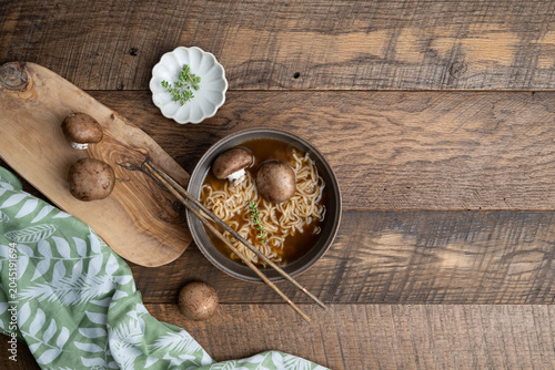 Hot noodle pho soup with whole, baby portabella mushrooms, noodles and thyme on a wooden table with green and white napkin towel and chopsticks
