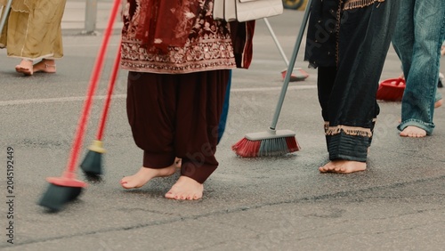 Indian female cleaners sweep the street with brooms during the Sikh procession