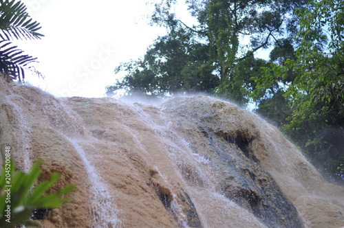A waterfall is pouring water down a rocky hill. The water is white and the rocks are brown. The scene is peaceful and serene