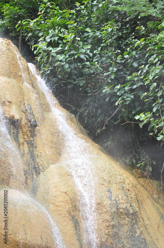 A waterfall is flowing down a rocky cliff. The water is clear and the rocks are brown. The scene is peaceful and serene