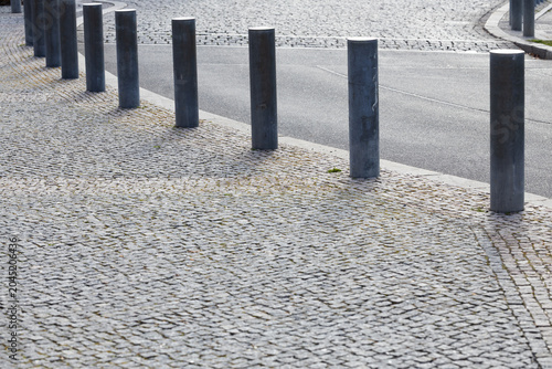 Tableau sur toile Series of metal bollards lining a curved cobblestone pathway adjacent to a smoot