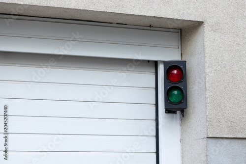 Photos Traffic light with red and green signals mounted on a wall next to a closed gara
