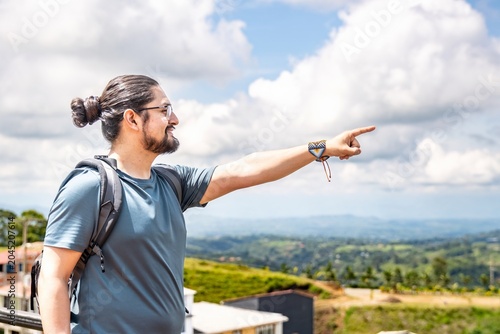 Man with backpack pointing at scenic green mountain valley
