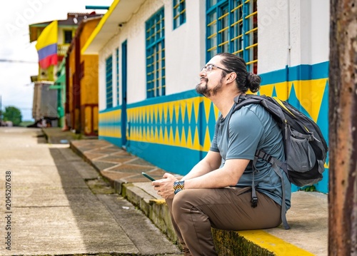 Man with backpack looking up holding phone on colorful street