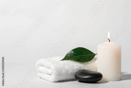 Spa setup with white towel, candle and black stone at the light grey background. Copy space