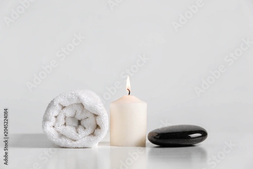 Spa setup with white towel, candle and black stone at the light grey background. Copy space