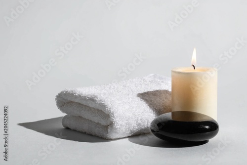 Spa setup with white towel, candle and black stone at the light grey background. Copy space