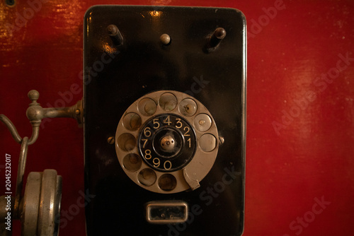 Close-up photograph of a vintage black rotary dial telephone mounted against a red background.