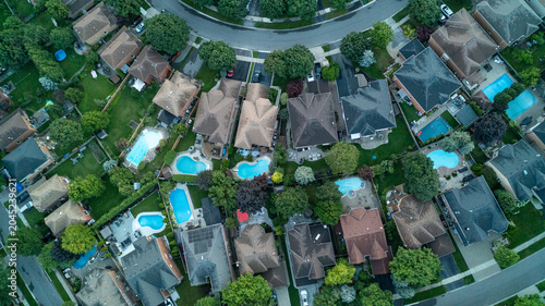 Foto A direct overhead drone photograph capturing a row of residential suburban homes situated along a curved street cul-de-sac, featuring multiple backyard swimming pools and manicured green lawns