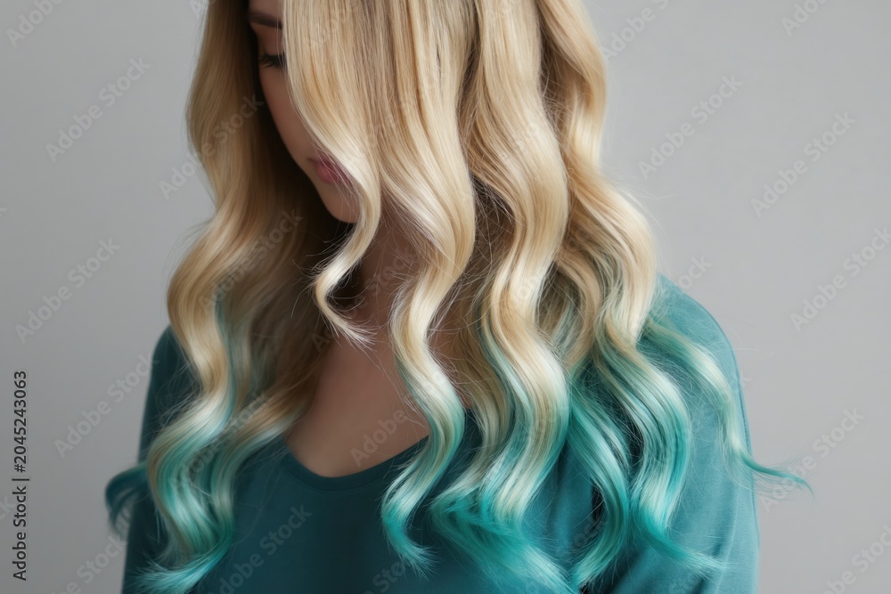 Fototapeta premium Woman displays wavy blonde hair with teal ombre ends. Hair stylists use for color trends. Beauty salons promote new looks. Fashion ads feature hair color. Models show off unique hair dyes. Creative