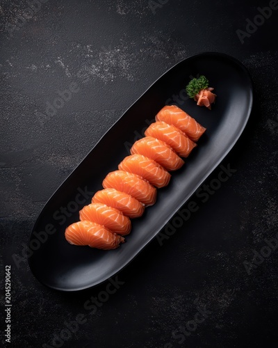 Elegant salmon sashimi arrangement on black plate with minimal garnish