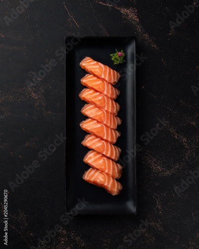 Elegant salmon sashimi arrangement on black plate with minimal garnish