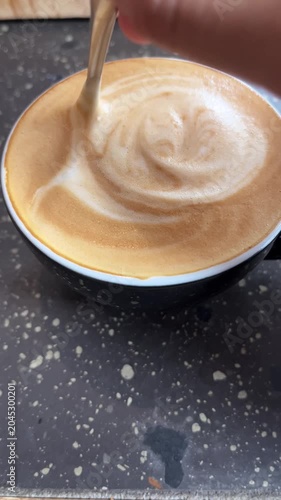 Hand stirring creamy frothy coffee in black cup on marble surface