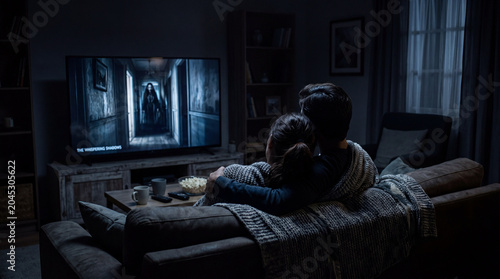 Couple watching scary movie at night on couch with popcorn