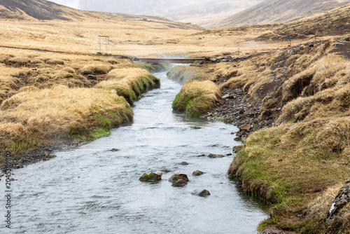 Photos Geothermal stream with rising steam vents flowing through a grassy valley in Rey