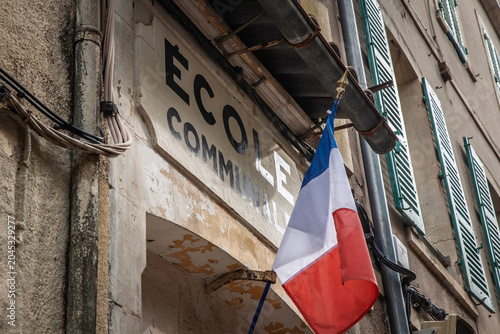 French flag hanging in front of an ecole communale, meaning primary school in french, in France, showing signage linked to local public education and the school system.