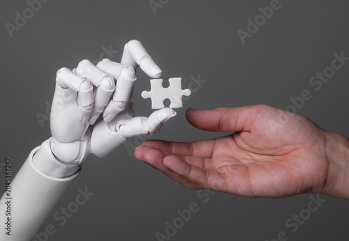 Robot hand passing a jigsaw puzzle piece to a human hand.