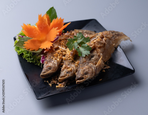 Deep fried fish topped with crispy garlic on black plate close up.