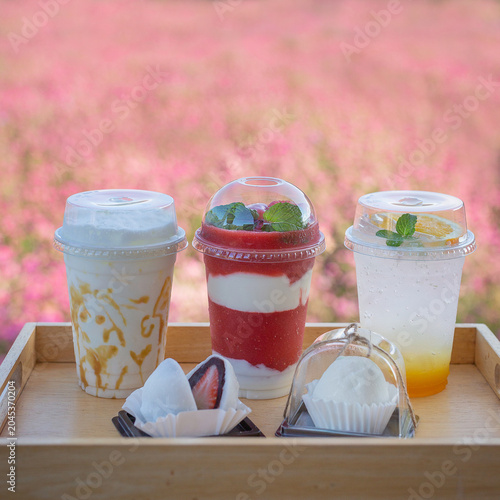 Traditional Japanese strawberry daifuku mochi cut in half showing fresh strawberry filling, served with a refreshing iced orange drink on a wooden table in a purple flower field.