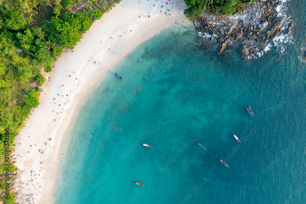 Obraz premium People relax on the white sand beach and swim in the clear blue ocean water beside lush jungle on Patong Beach, Phuket, Thailand during vacation