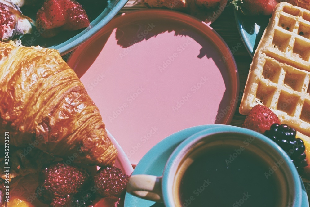Naklejka premium Pink surface copy space surrounded by a breakfast border of croissant, waffle and coffee for brunch cafe menu marketing, morning food blog and bakery social media