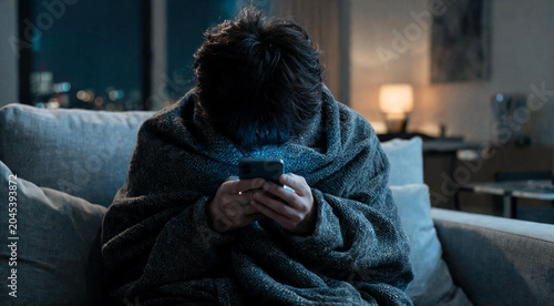 Over shoulder view of millennial girl using smartphone in dark apartment dealing with digital fatigue and insomnia