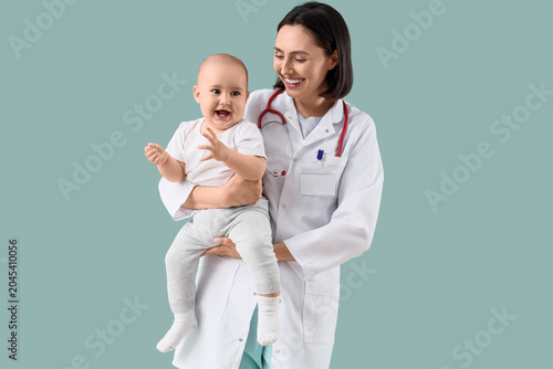 Young female pediatrician with happy little baby on green background