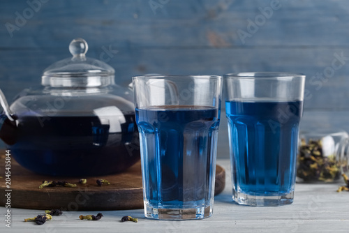 Foto Glasses and teapot of butterfly pea flower tea on blue wooden background