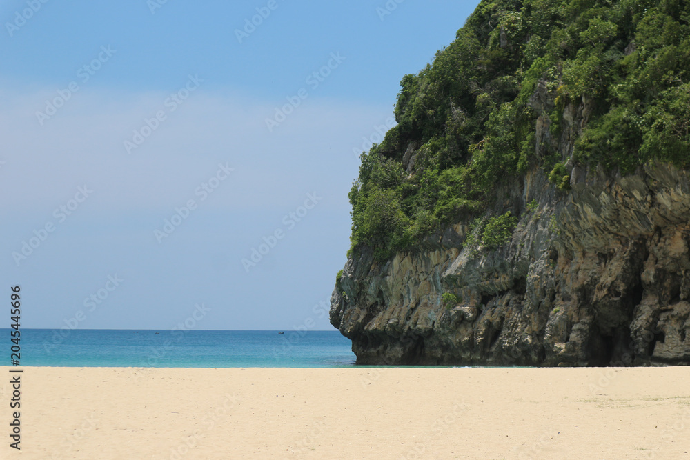 Naklejka premium Scenic tropical beach with white sand and large rocky cliff covered in green trees