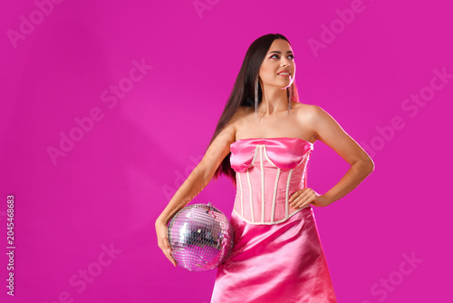 Stylish young woman with disco ball on violet background