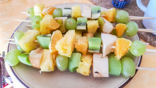 Foto Colorful fruit skewers featuring pineapple, kiwi, and grapes on a white plate