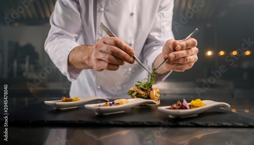 Professional chef using tweezers to garnish appetizers in restaurant kitchen