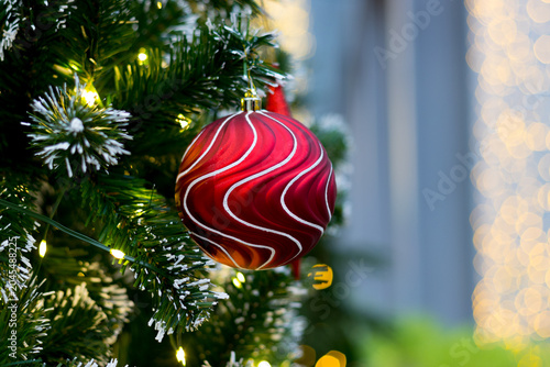 red ornament ball hanging on christmas tree. blurry golden light curtain backdrop on the right side