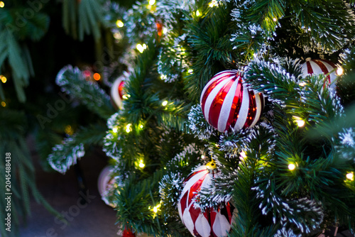 shiny red swirl ornament hanging on green pine branch with snow. warm fairy lights glowing around. festive holiday season